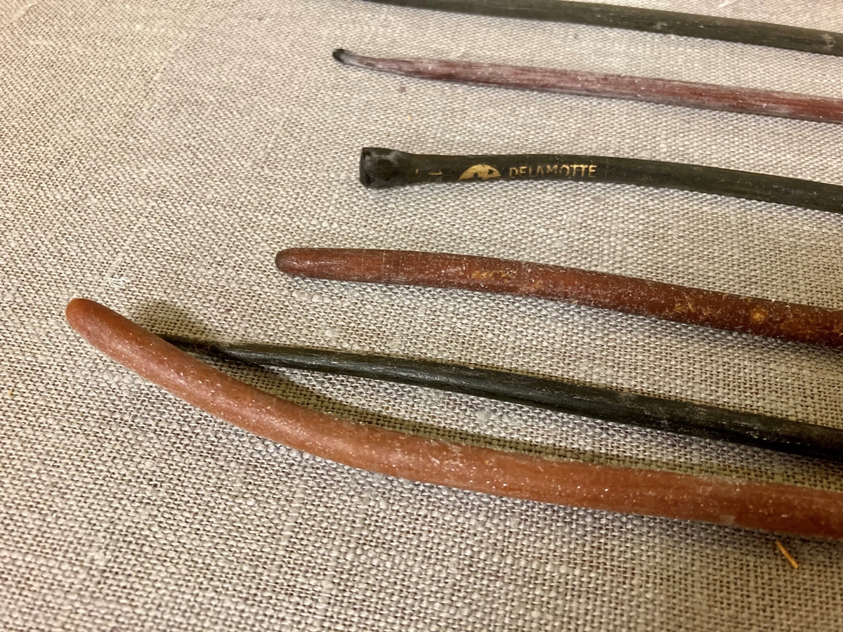 11 avlange pinneformede instrumenter i et gummilignende materiale. Bredere i den ene enden. Oppbevart i et glassrør.