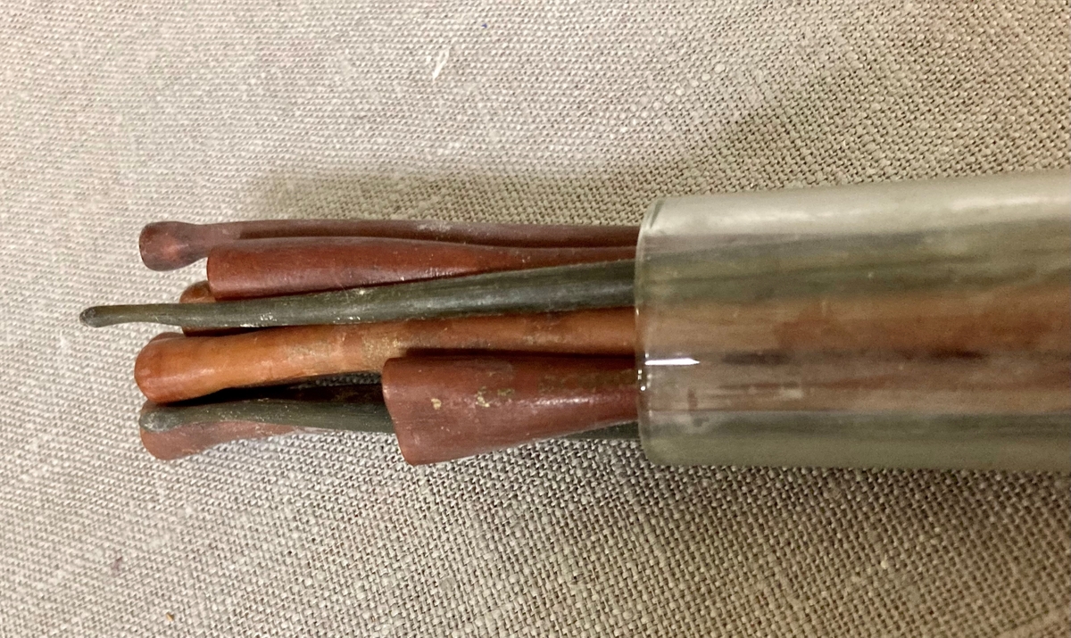 11 avlange pinneformede instrumenter i et gummilignende materiale. Bredere i den ene enden. Oppbevart i et glassrør.