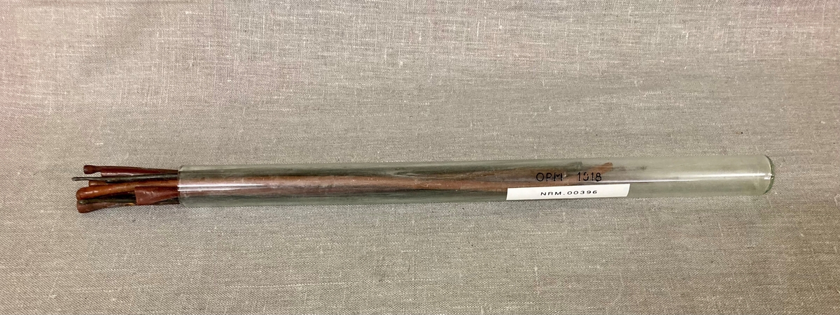 11 avlange pinneformede instrumenter i et gummilignende materiale. Bredere i den ene enden. Oppbevart i et glassrør.