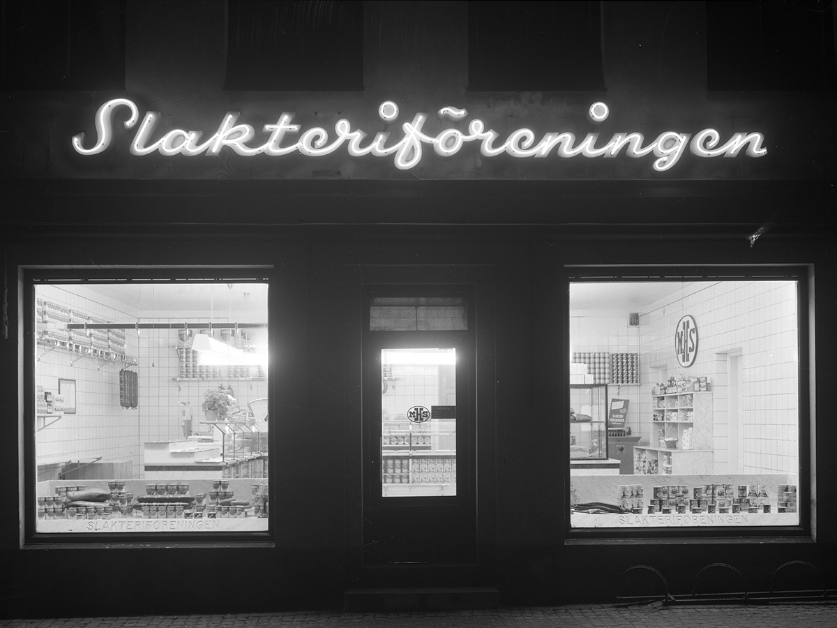 Skyltfönster till Slakteriföreningens butik på Borgmästaregatan, Varberg. "MHS" på dörren står för Mellersta Hallands slakteriförening. Förutom charkuterier säljs också konserver.