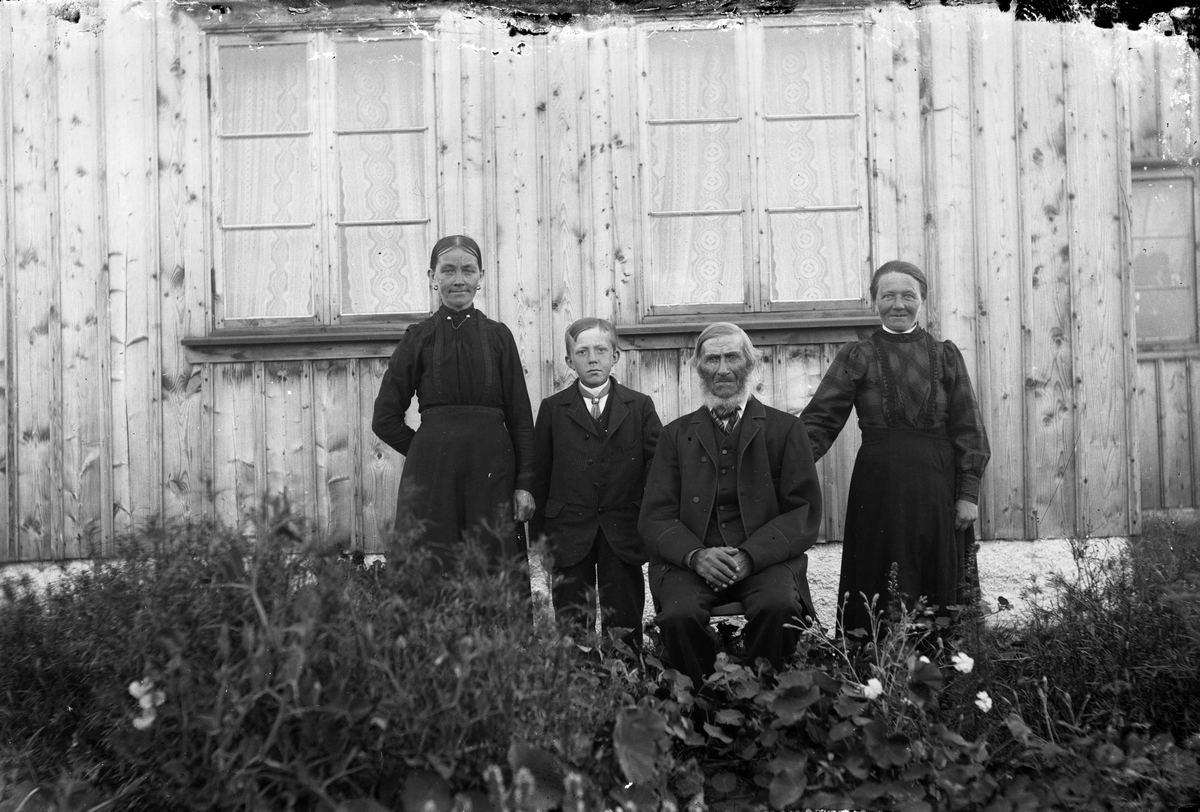 Sällstorp 3, Klingeberg. Fyra personer vid en rabatt med bland annat krasse och nejlikor framför bostadshusets omålade fasad. Åldermannen Magnus Olsson (född 1830) med yvig skepparkrans sitter på en stol med yngsta dottern Anna-Kristina till höger och på vänster sida sonhustrun Alma Kristina Gustafsdotter med sonen Ivar Magnusson.

Magnus Olsson köpte Klingeberg år 1868 (fotografens morfar Carl Engström ägde stället under några år men sålde det 1861). Magnus hade gift sej 1857 och flyttade dit från Derome med fru och fem barn. Här kom familjen att utökas med ytterligare tre barn. Sonen John gifte sig med Alma Kristina på bilden men avled redan vid 44 års ålder. Endast Ivar uppnådde vuxen ålder av deras fyra barn, övriga dog i unga år. Magnus däremot blev nästan 95 år.