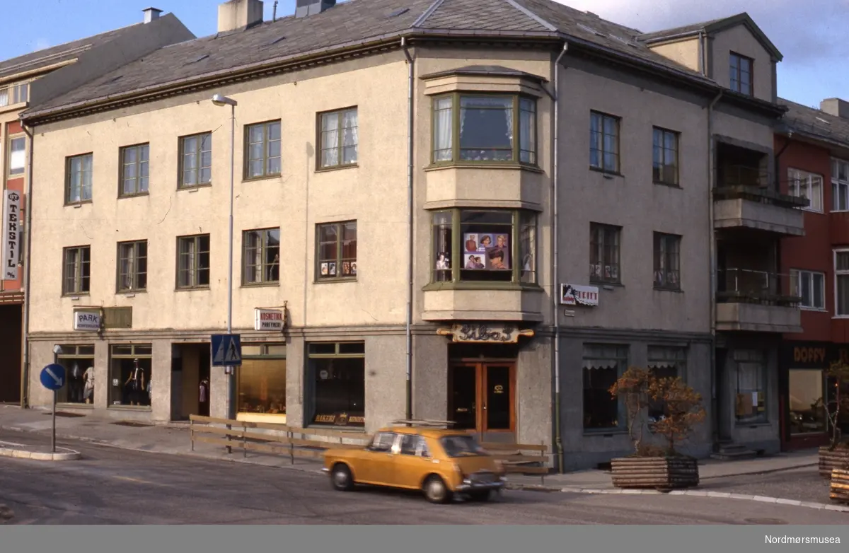 På hjørnet Langveien/Skolegata på Kirkelandet i Kristiansund, med bakeriet til Sibas. Datering er ikke kjent, men muligens på 1980-tallet. Fra Stein Magne Bach sin private fotosamling. Denne samlingen består av dias fra perioden omkring 1980. Fra Nordmøre museums fotosamlinger.