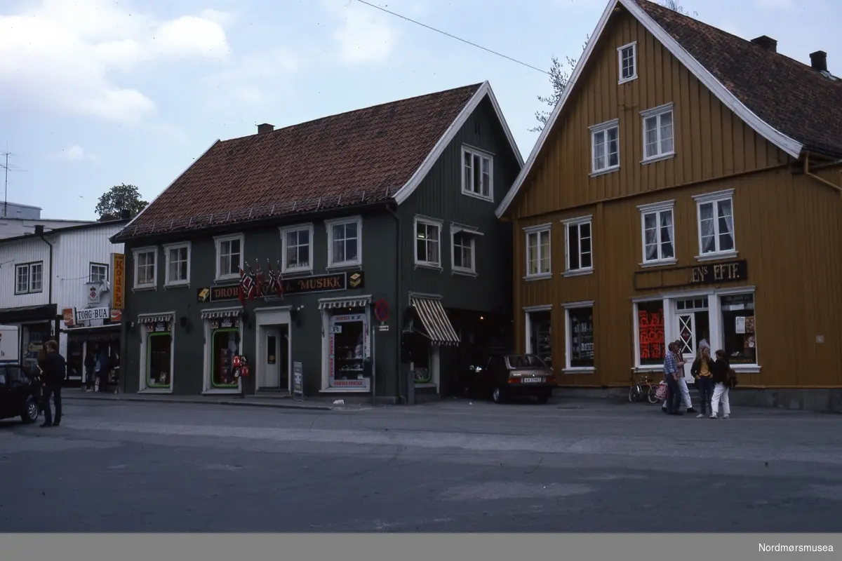 Foto trolig fra et gateparti i Drøbak i Frogn kommune i Viken fylke. Datering er trolig på 1980-tallet. Fra Stein Magne Bach sin private fotosamling. Denne samlingen består av dias fra perioden omkring 1980. Fra Nordmøre museums fotosamlinger.