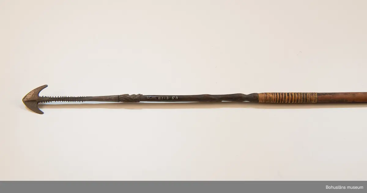 Kontinent: Afrika.

Ur lappkatalogen:
Pil, l. 94 cm. Spets av järn med två stora hullingar o. en mängd smärre. Skaftholk på sticka, instucken i skaftet o. surrad. Stickan försedd med skurna ornament o. två människoansikten i relief. 10 styrfjädrar, något vridna. Mangbetu el. Azande.

Uppgifter om E. Göransson i Knut Adrian Anderssons katalog samt historik om samlingen: Se UM61.3.1