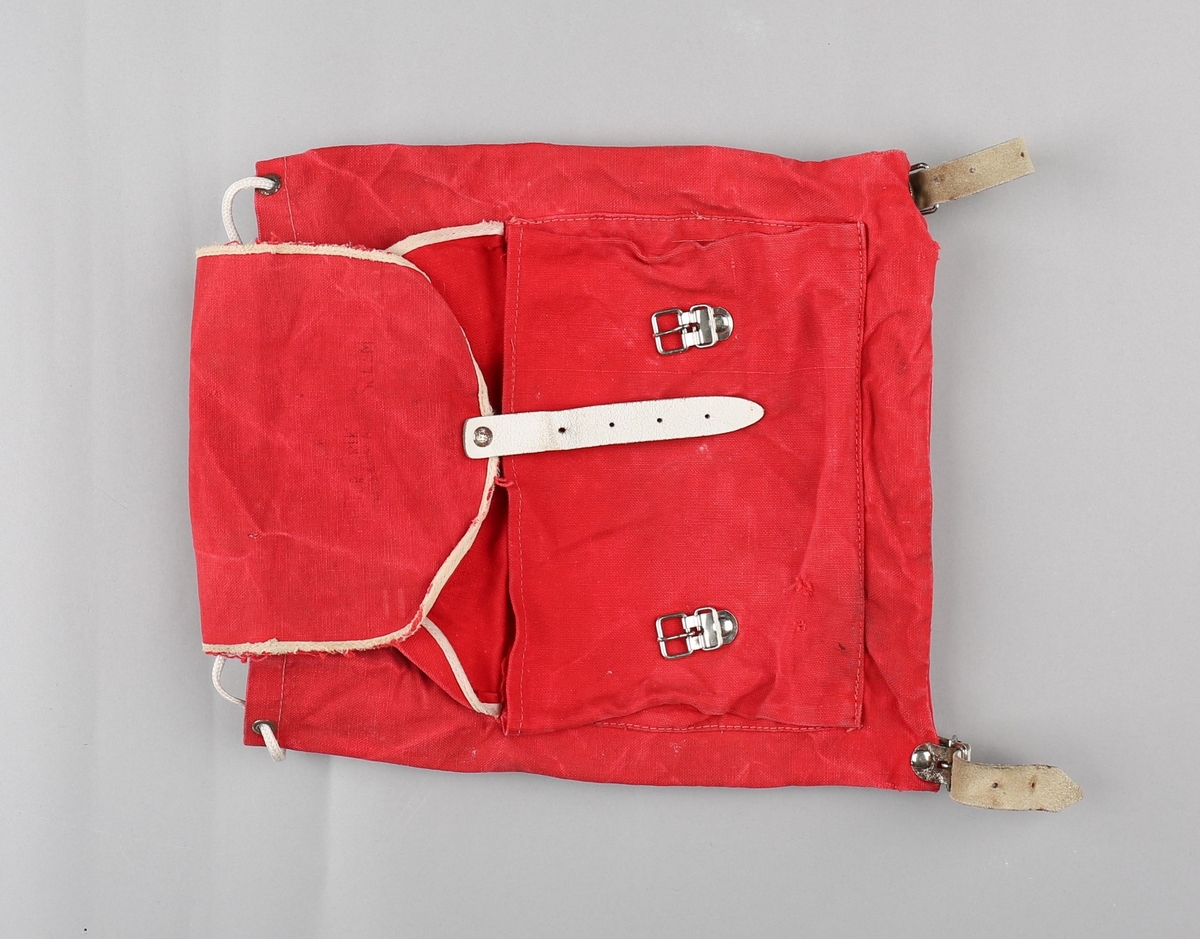 Ryggsekk for barn. Sekken er produsert i bomullstekstil. Rektangulær poseform med opning  toppen. På framsida er det påsydd lomme med klaff, lukka med to spenner og lérreimar. Hol med maljer i opninga, med snorknyting. Klaff over opninga er sydd fast i bakkant, har runda form i framkant og lukking med spenne og lérreim. Oppe på ryggen festa to selar i lér som er festa til metallspenner nede på sekken. Lommeklaff og toppklaff er kanta med kvitt skråband