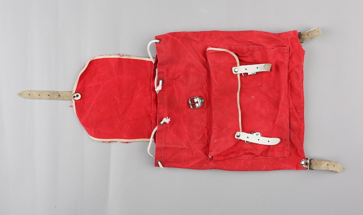 Ryggsekk for barn. Sekken er produsert i bomullstekstil. Rektangulær poseform med opning  toppen. På framsida er det påsydd lomme med klaff, lukka med to spenner og lérreimar. Hol med maljer i opninga, med snorknyting. Klaff over opninga er sydd fast i bakkant, har runda form i framkant og lukking med spenne og lérreim. Oppe på ryggen festa to selar i lér som er festa til metallspenner nede på sekken. Lommeklaff og toppklaff er kanta med kvitt skråband