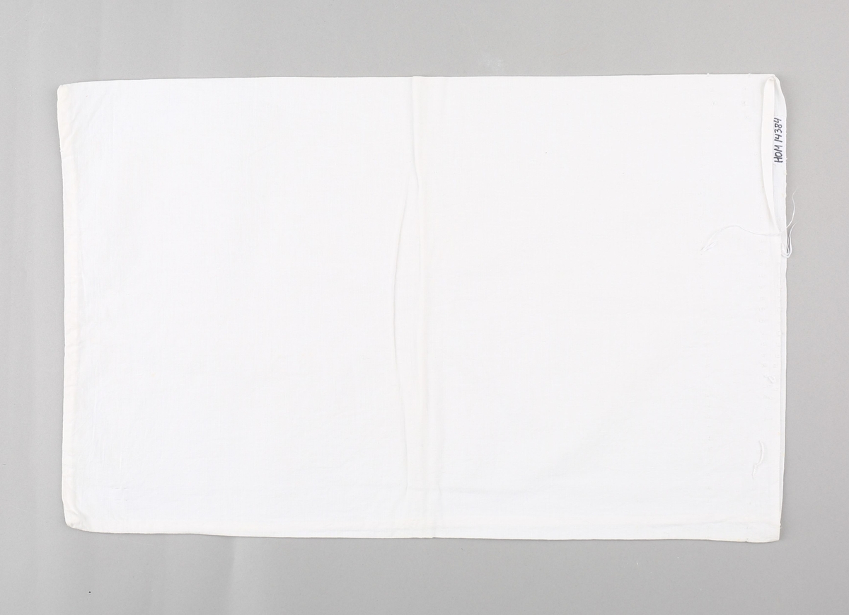 Sukkersekk nytta som putevar til barneseng. Rektangulært stykke bomullstekstil i lerretsvevnad, bretta i to på langs. Sydd saman med maskinsaum langs eine kortenden og eine langsida. Jarekant i opningsenden med spor etter sting og restar av bomullstråd nytta til å sy saman sukkersekken.