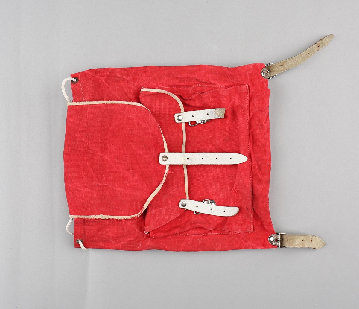 Ryggsekk for barn. Sekken er produsert i bomullstekstil. Rektangulær poseform med opning  toppen. På framsida er det påsydd lomme med klaff, lukka med to spenner og lérreimar. Hol med maljer i opninga, med snorknyting. Klaff over opninga er sydd fast i bakkant, har runda form i framkant og lukking med spenne og lérreim. Oppe på ryggen festa to selar i lér som er festa til metallspenner nede på sekken. Lommeklaff og toppklaff er kanta med kvitt skråband