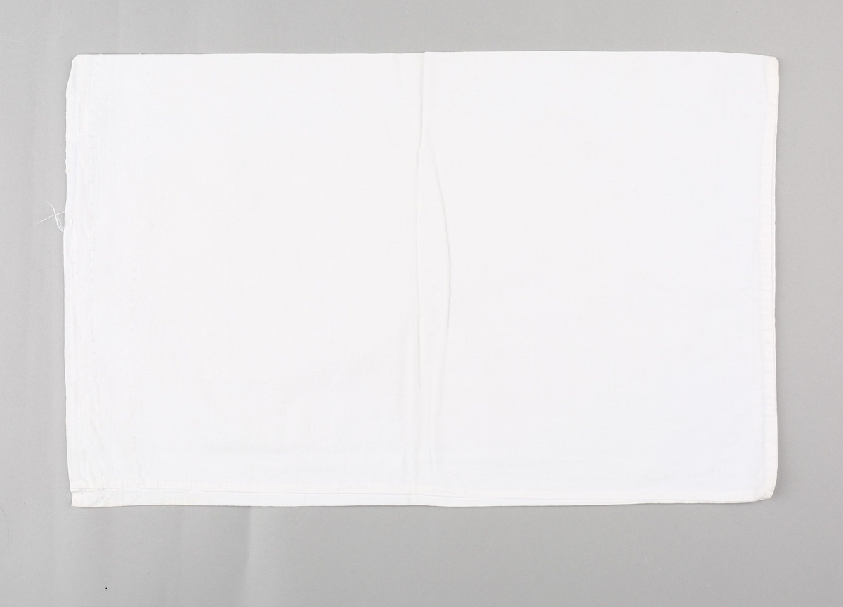 Sukkersekk nytta som putevar til barneseng. Rektangulært stykke bomullstekstil i lerretsvevnad, bretta i to på langs. Sydd saman med maskinsaum langs eine kortenden og eine langsida. Jarekant i opningsenden med spor etter sting og restar av bomullstråd nytta til å sy saman sukkersekken.