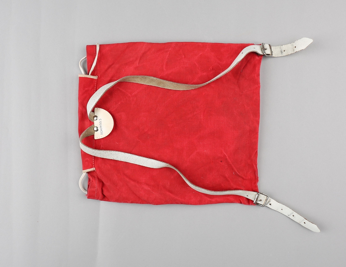 Ryggsekk for barn. Sekken er produsert i bomullstekstil. Rektangulær poseform med opning  toppen. På framsida er det påsydd lomme med klaff, lukka med to spenner og lérreimar. Hol med maljer i opninga, med snorknyting. Klaff over opninga er sydd fast i bakkant, har runda form i framkant og lukking med spenne og lérreim. Oppe på ryggen festa to selar i lér som er festa til metallspenner nede på sekken. Lommeklaff og toppklaff er kanta med kvitt skråband