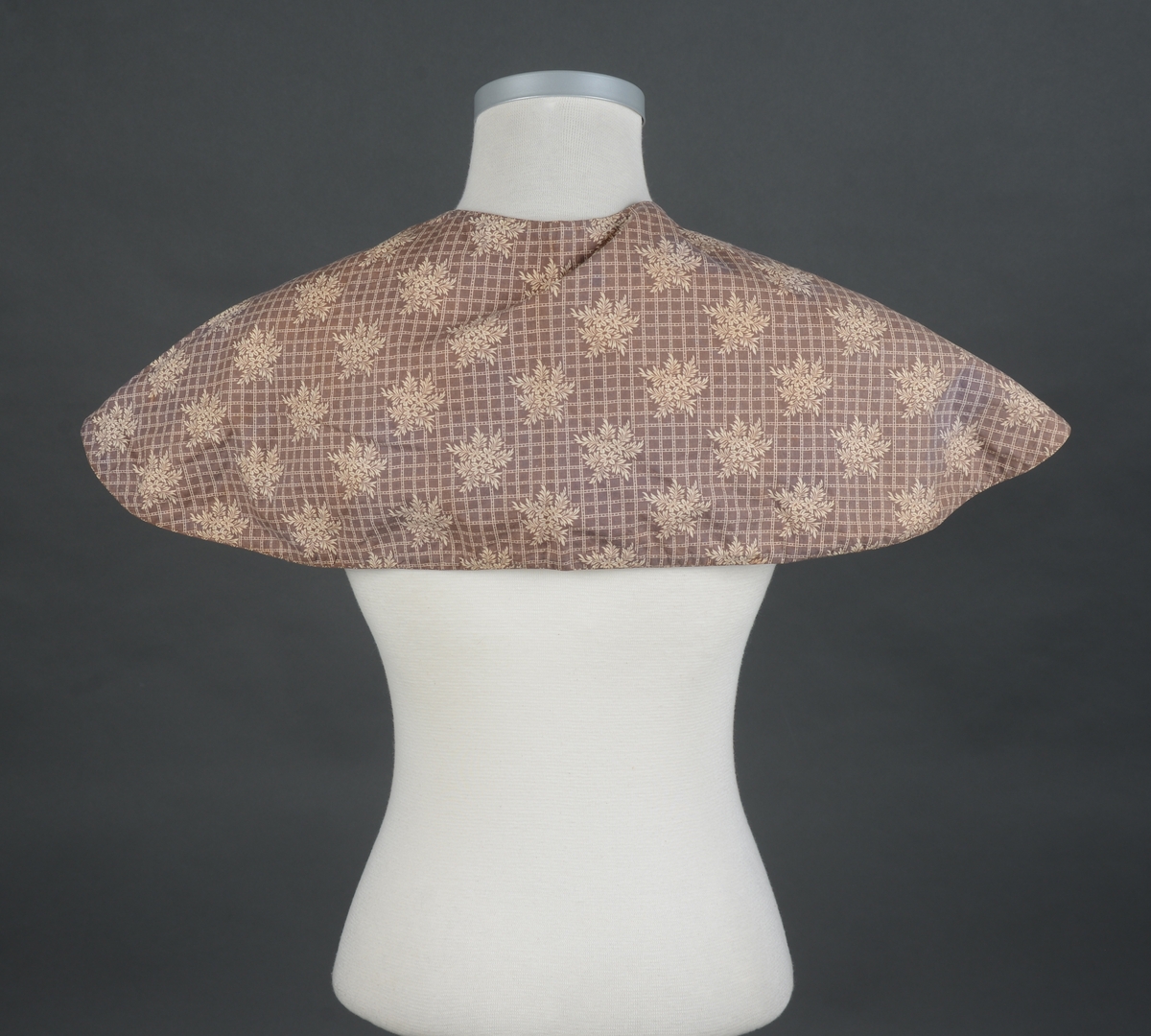 Kappe, stor krage sydd av tynt blankt trykt bomullstoff/kattunstoff. Helfora med ubleika bomullstoff. Lukning med hekte og trådhempe i halsen. Kappen er vrangsydd med tittekant. Hovedstoffet er skjøtt på flere steder.
Registrert som friserkappe i 1973. Det kan like gjerne være del av en draktdel.