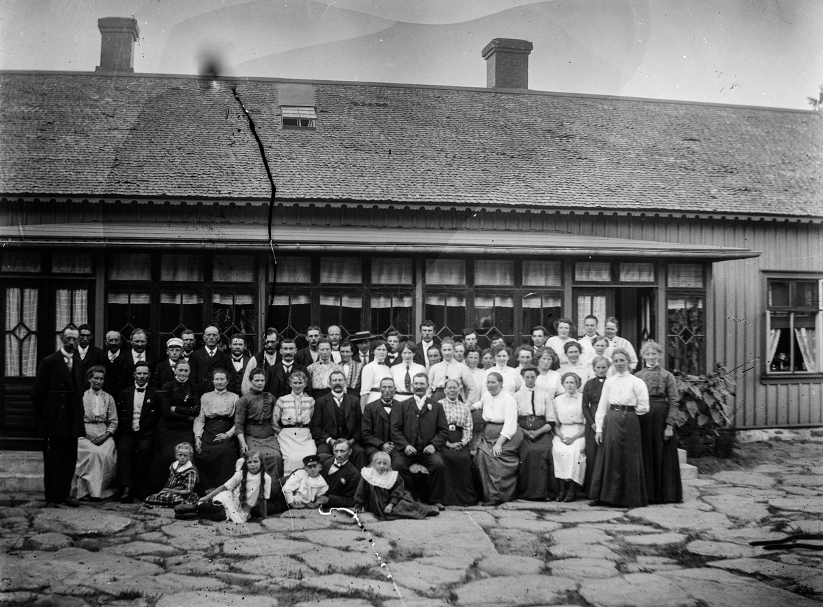 "Kalasfolk" i olika åldrar samlade framför en mycket långsträckt glasveranda med två ingångar. Bertha Engström (fotografens mor) sitter som tredje person från vänster. En man och fyra barn ligger främst, direkt på stenläggningen. Huset har en smal figursågad dekorlist under takfoten och ett litet takfönster mellan skorstenarna. Meddela oss gärna om du vet vad gården heter!
(Bilden har diverse skador)