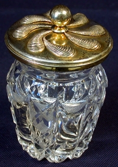 Material 3: Silver.
 :1 Cylinderformad burk av genomskinligt kristallglas med öppningens kant något utåtställd. Utsidans yta dekorerad med rutmönster och andra mönster i relief. Diameter i öppning: 68 mm, höjd med lock: 115 mm, djup: 83 mm.
   :2 Runt lock av silver, på mitten en knopp med vilken man lyfter av och sätter på locket. På ovansidan snäckformade dekorationer i relief.