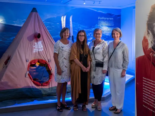 Fire damer står foran det lyserøde 90 grader syd teltet, de smiler inn i kamera.