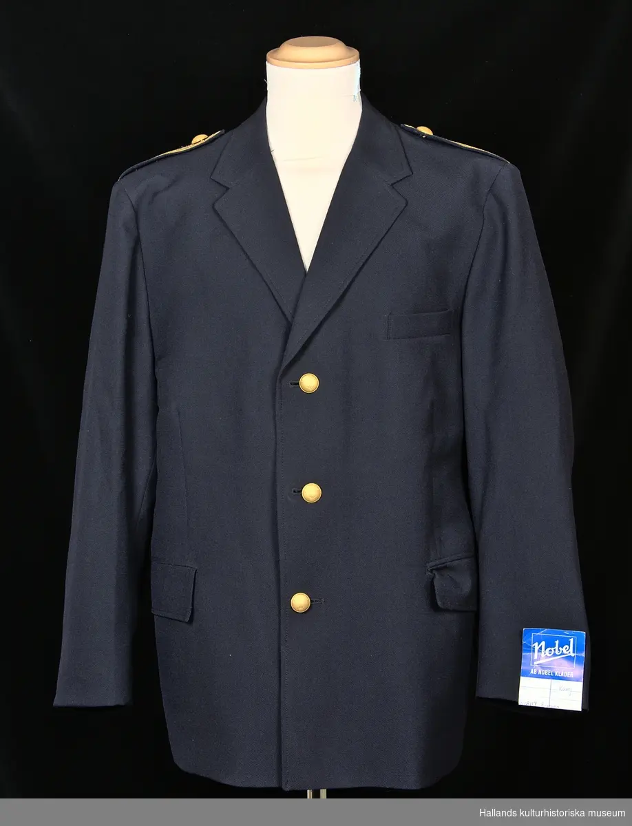 Uniformskavaj för tulltjänsteman

Enkelknäppt uniformskavaj av marinblå polyester- och ylleväv i kypert. Försedd med 3 gulmetallknappar dekorerade med vapensköld (tre kronor). Två fickor längs sidorna samt en bröstficka och två innerfickor. Fodrad med marinblått satintyg. På kavajens insida (vid vänstra bröstet) finns etikett: "KUNGL. HOVL. ESPECIALL MADE BY NOBEL. POLYESTER - ULL", samt tvättanvisningar. Axelklaffar grupp VII enligt 1979 års uniformsbestämmelser.