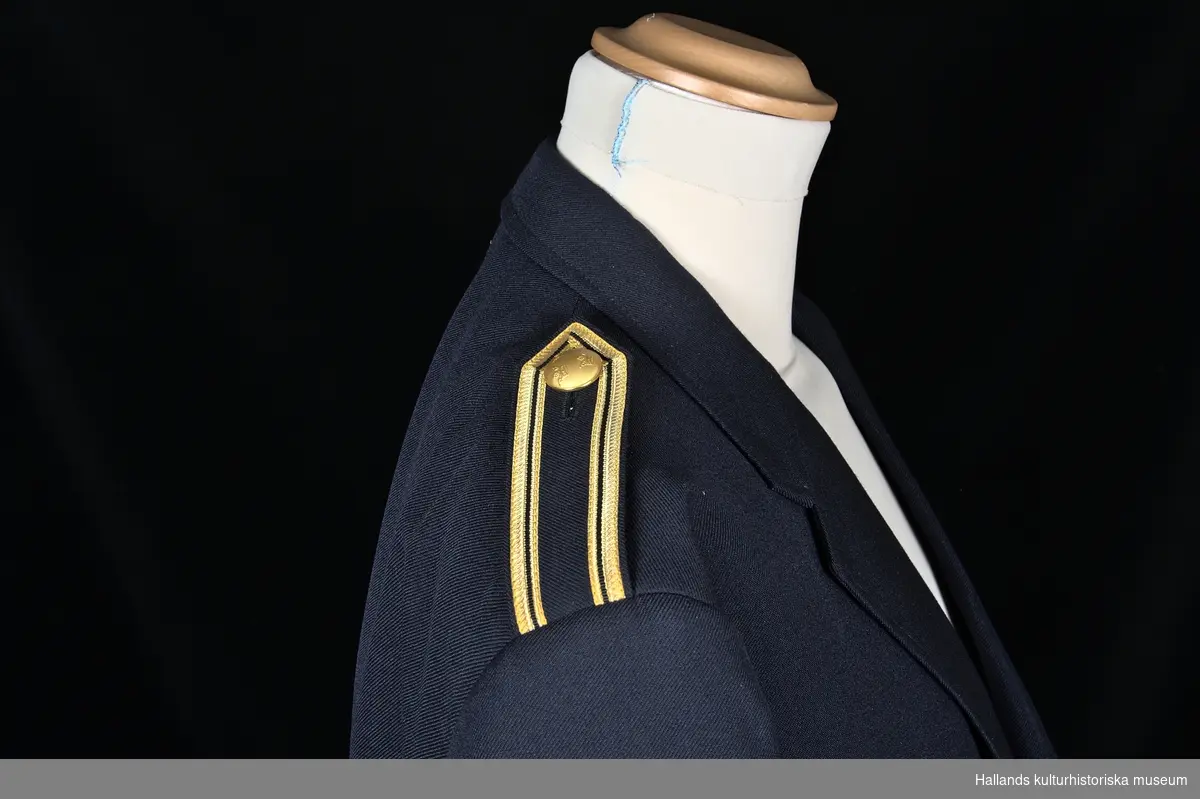 Uniformskavaj för tulltjänsteman

Enkelknäppt uniformskavaj av marinblå polyester- och ylleväv i kypert. Försedd med 3 gulmetallknappar dekorerade med vapensköld (tre kronor). Två fickor längs sidorna samt en bröstficka och två innerfickor. Fodrad med marinblått satintyg. På kavajens insida (vid vänstra bröstet) finns etikett: "KUNGL. HOVL. ESPECIALL MADE BY NOBEL. POLYESTER - ULL", samt tvättanvisningar. Axelklaffar grupp VII enligt 1979 års uniformsbestämmelser.