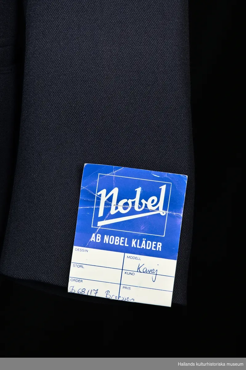 Uniformskavaj för tulltjänsteman

Enkelknäppt uniformskavaj av marinblå polyester- och ylleväv i kypert. Försedd med 3 gulmetallknappar dekorerade med vapensköld (tre kronor). Två fickor längs sidorna samt en bröstficka och två innerfickor. Fodrad med marinblått satintyg. På kavajens insida (vid vänstra bröstet) finns etikett: "KUNGL. HOVL. ESPECIALL MADE BY NOBEL. POLYESTER - ULL", samt tvättanvisningar. Axelklaffar grupp VII enligt 1979 års uniformsbestämmelser.