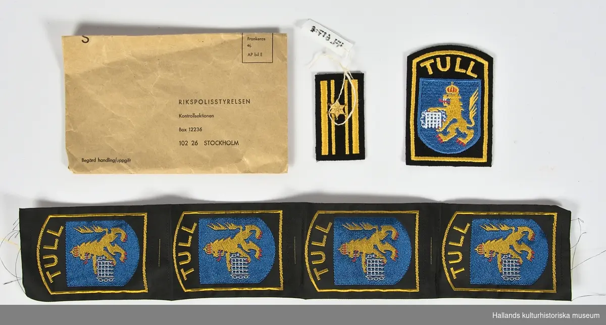 Uniformsmärken till tulluniform. Från 1984 eller 1986 års utförande. Grupp VI.

a) Kuvert. Adresserad från Rikspolisstyrelsen. Brunt papper. Text: se bild.

b) Tygmärke. Tullverkets heraldiska vapen i vit, blå, gul och röd tråd. Vapnet är omgärdat av en guldfärgad bård samt texten "TULL" i välvt typsnitt på tygmärkets överdel.

c) Tygremsa. Fyra stycken märken föreställande tullverkets heraldiska vapen i vit, blå, gul och röd tråd. Vapnet är omgärdat av en guldfärgad bård samt texten "TULL" i välvt typsnitt på emblemens överdel.

d) Tygmärke. Gradbeteckning från 1984 eller1986 års uniformsbestämmelse (Grupp VI). Kombineras med mässingsstjärna (e).

e) Mässingstjärna i gulmetall. Fästes på Tygmärke (d)