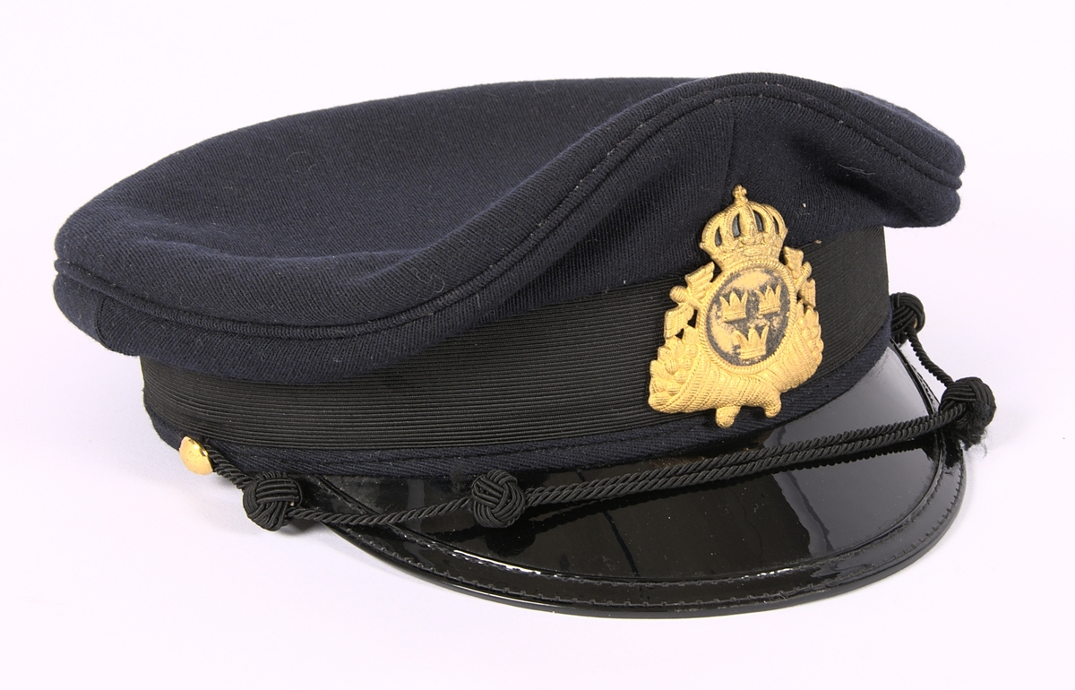 Uniform för tulltjänsteman. Komplett - utöver gradbeteckningar på kavajen - med kavaj, väst, byxor och mössa. I kavajens ficka fanns även ett mössemblem och en knapp i gulmetall.

a) Dubbelknäppt kavaj av marinblå polyester/ylle. Försedd med 8 gulmetallknappar dekorerade med vapensköld i form av tre kronor. Två fickor framtill.

b) Väst av marinblått ylle. Enkelknäppt. Försedd med 6 stycken gulmetallknappar dekorerade med vaptensköld i form av tre kronor. Fyra infällda fickor på framkanterna. Backstycke av svart satintyg.

c) Byxor av marinblå polyester/ylle. Två fickor framtill.

d) Uniformsmössa av av marinblå polyester/ylle. Skärm av svart lack. Framtill sitter en svart snodd som är fäst vid var sida av mössan med knapp av gulmetall. I mössans mitt tullverkets emblem i guldbrodyr enligt 1969 års reglemente. Fodrad med svart satintyg samt ett band av brunt konstläder. Ett emblem finns på mössans insida: "HB", samt storlek: 55.

e) Mössemblem (Tullverket) bestående av en metallskiva klädd med ylletyg. Broderad med guldtråd. Enligt 1949 års reglemente. Fanns placerad i kavajens ficka.

f) Knapp i gulmetall. Svagt välvd form. Försedd med en krona i relief. Kronan är omgärdad av texten: "Kungl. Tullverket". På baksidan av knappen sitter en ögla.