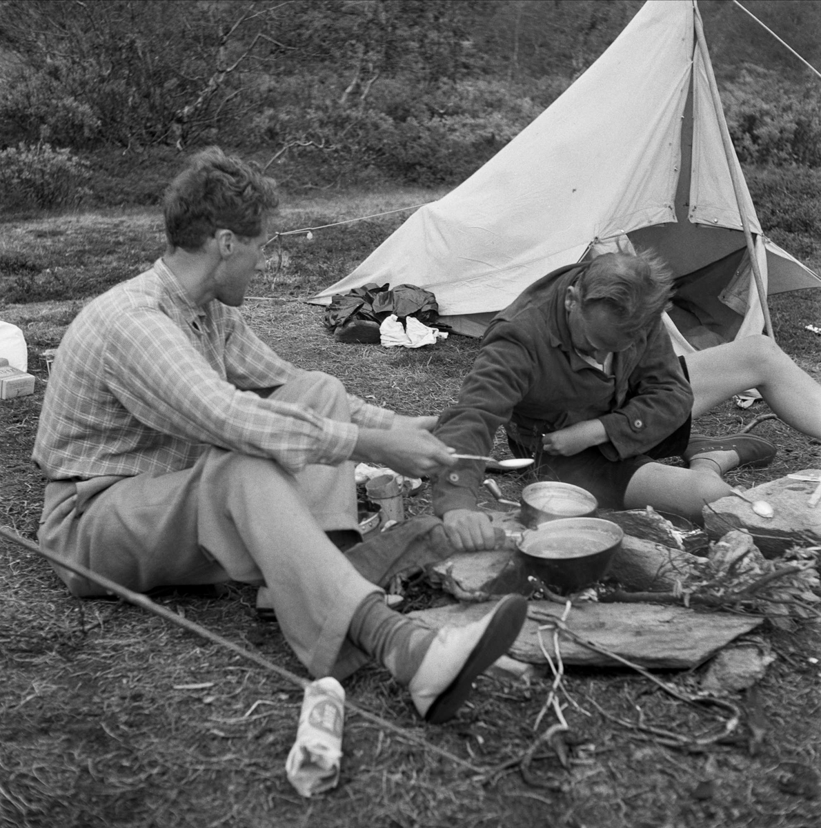 Dag Hammarskjöld och Sverker Åström på fjällvandring på Sulitelma. Två män har slagit läger och rest tält. Nu lagar de mat över eld.