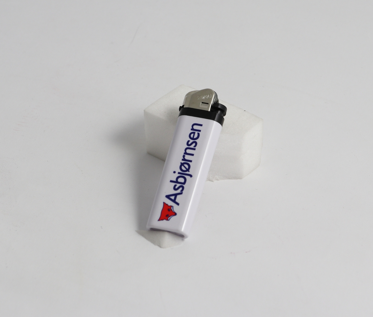 Hvit plast tank med revelogo og skriften "Asbjørnsen" på den ene siden, skriften "Eventyr 3" på andre siden. Tennmekanisme på toppen bestående av metall og svartplast.