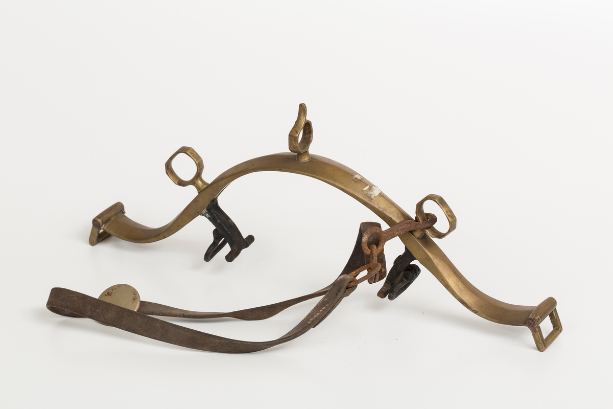 Høvre i smidd stål trukket med messing med påloddete messingringer/-fester. Stykke av lærrem festet med D-ring, lenkeledd og karabinkrok til messingring på høvret. Rund messingplate med bøyle er tredd inn på reimen.