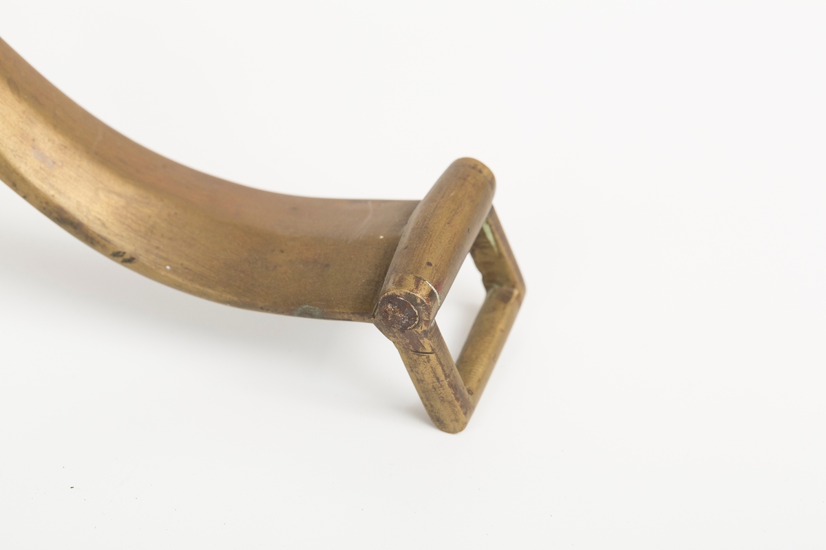 Høvre i smidd stål trukket med messing med påloddete messingringer/-fester. Stykke av lærrem festet med D-ring, lenkeledd og karabinkrok til messingring på høvret. Rund messingplate med bøyle er tredd inn på reimen.