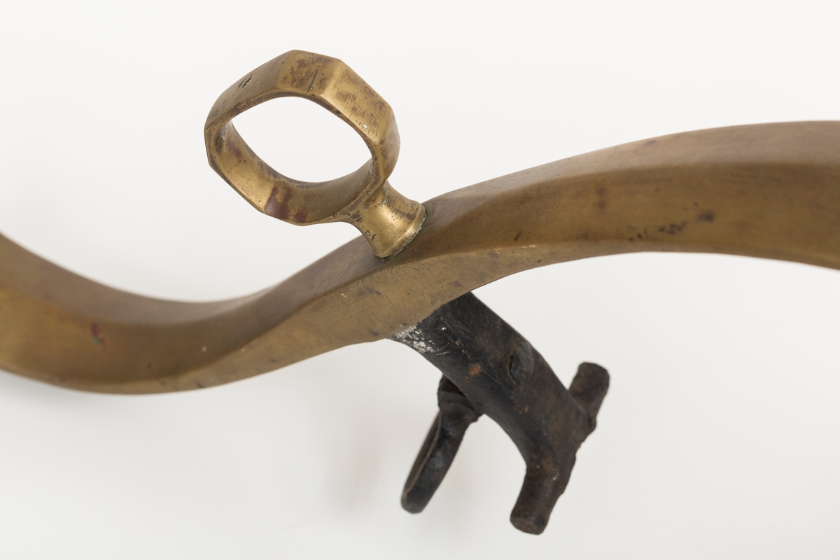 Høvre i smidd stål trukket med messing med påloddete messingringer/-fester. Stykke av lærrem festet med D-ring, lenkeledd og karabinkrok til messingring på høvret. Rund messingplate med bøyle er tredd inn på reimen.