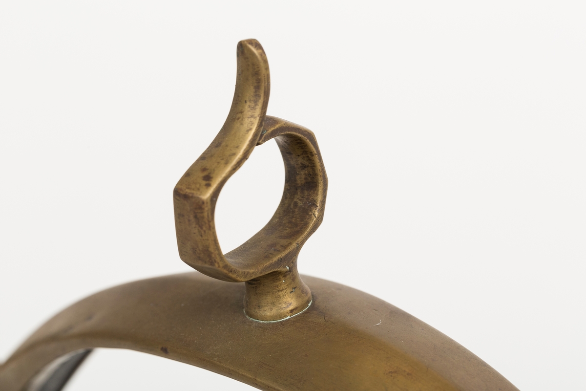 Høvre i smidd stål trukket med messing med påloddete messingringer/-fester. Stykke av lærrem festet med D-ring, lenkeledd og karabinkrok til messingring på høvret. Rund messingplate med bøyle er tredd inn på reimen.