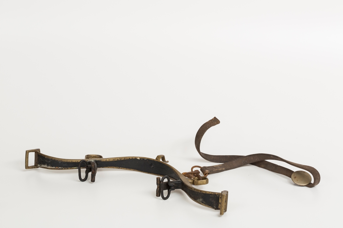 Høvre i smidd stål trukket med messing med påloddete messingringer/-fester. Stykke av lærrem festet med D-ring, lenkeledd og karabinkrok til messingring på høvret. Rund messingplate med bøyle er tredd inn på reimen.