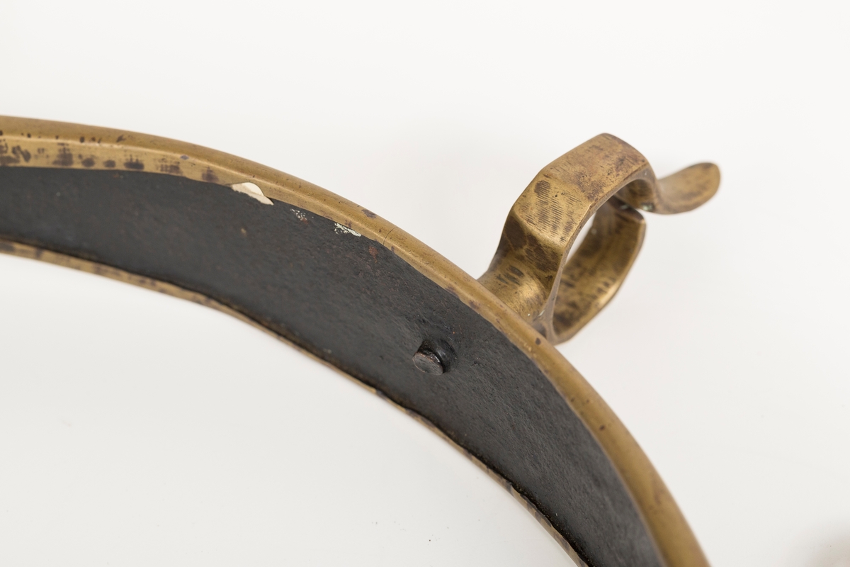 Høvre i smidd stål trukket med messing med påloddete messingringer/-fester. Stykke av lærrem festet med D-ring, lenkeledd og karabinkrok til messingring på høvret. Rund messingplate med bøyle er tredd inn på reimen.