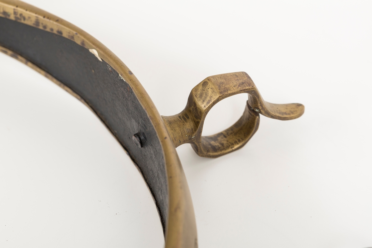 Høvre i smidd stål trukket med messing med påloddete messingringer/-fester. Stykke av lærrem festet med D-ring, lenkeledd og karabinkrok til messingring på høvret. Rund messingplate med bøyle er tredd inn på reimen.