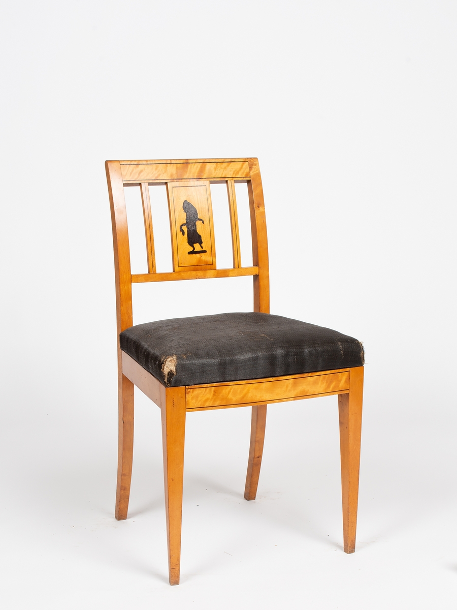 12 stk. like stoler i empire stil (A-L). Lys polert bjerk, negativ mørk intarsia i lyst ryggbrett. Rett sete avsmalnende baktil, stoppet og trukket m/ sort hestehårstrekk. Firsidige rette ben, bakbenene svakt utsvunge. Forsidens sarg svakt buet. Svakt buet akterstaver, rett skulderbrett og tverrspross. Mellom disse, bredt ryggbrett flankert av 2 smale spiler. Langs kantene på ryggbrett, skulderbrett og forsidens sarg, mørk konturstripe i intarsia.