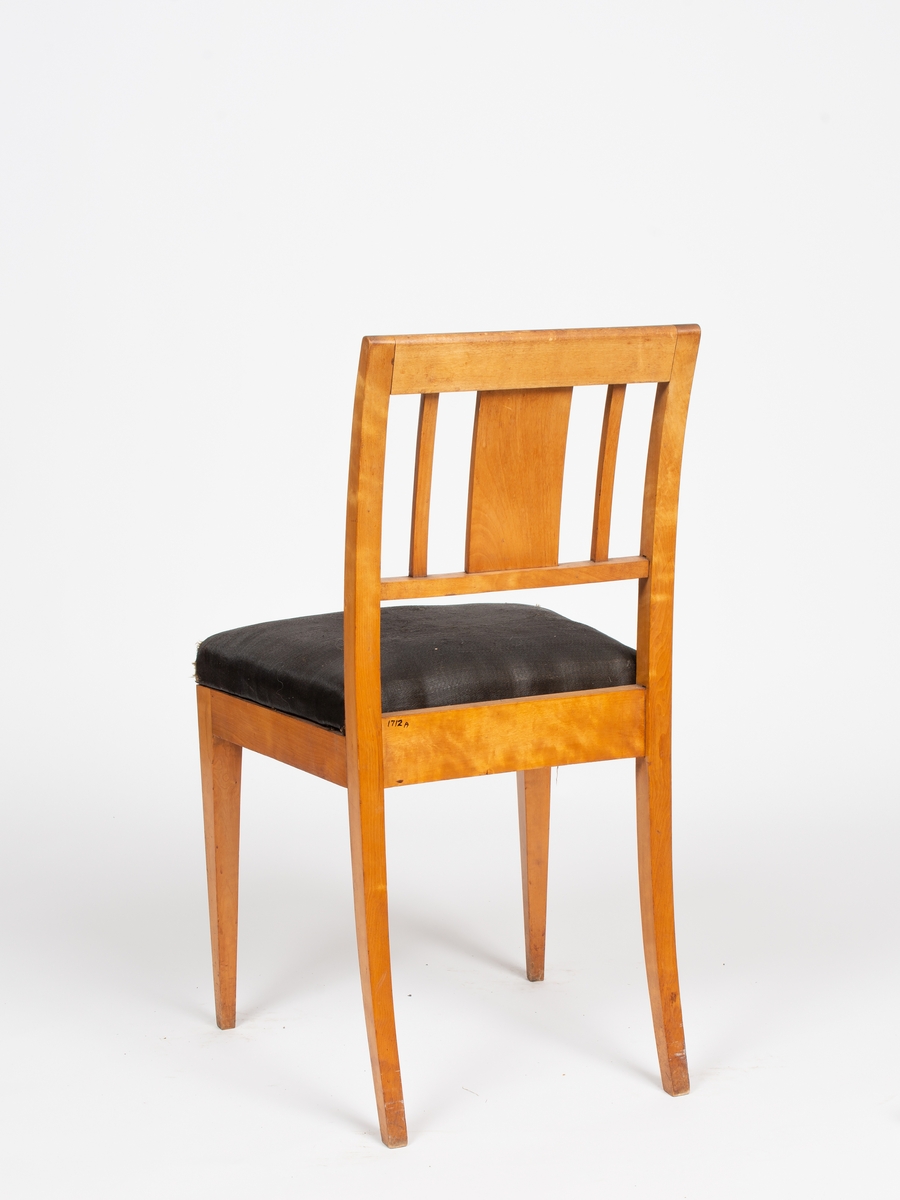 12 stk. like stoler i empire stil (A-L). Lys polert bjerk, negativ mørk intarsia i lyst ryggbrett. Rett sete avsmalnende baktil, stoppet og trukket m/ sort hestehårstrekk. Firsidige rette ben, bakbenene svakt utsvunge. Forsidens sarg svakt buet. Svakt buet akterstaver, rett skulderbrett og tverrspross. Mellom disse, bredt ryggbrett flankert av 2 smale spiler. Langs kantene på ryggbrett, skulderbrett og forsidens sarg, mørk konturstripe i intarsia.