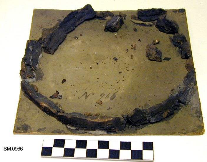 Stor rund kittring i fragmenter. Et lite stykke sammensmeltet jern kom også til dette nr. Disse saker (TGM-SM.0965-0966) ble funnet sammen, under tre steiner. Leirkaret inneholder aske, kull og brente bein. Datering usikker, mulig keltertid eller overgangen til romertid.
