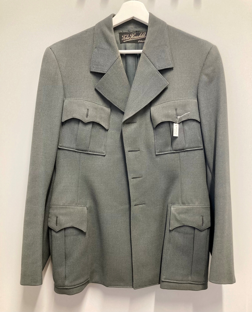 Grågrønn uniform med liggende krave og fire lommer, ridebukse og skilue (Finn Quales modell). Uniformen har bruksmerker, særlig på kraven. Luen er slitt, foret har løsnet. Alle gradstegn og knapper er fjernet fra jakken. God kvalitet på stoffet, muligens offisersuniform. (NB: Fremstår som grå på bildene, men har i virkeligheten en blass militærgrønn farge.)