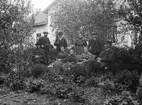 Familjen Hedrén med sällskap i trädgården till Viby skolhus, som även inrymde kantorsbostad. Året är omkring 1905 och Karl August Hedrén har varit socknens organist och skollärare sedan 1891. Vi ser honom skäggprydd till vänster i bild. På bänken sitter hustrun Elin Elfrida med parets yngsta barn vid sin sida och bakom bänken står deras två äldsta. Övriga personers identiteter har inte kunnat klarläggas.