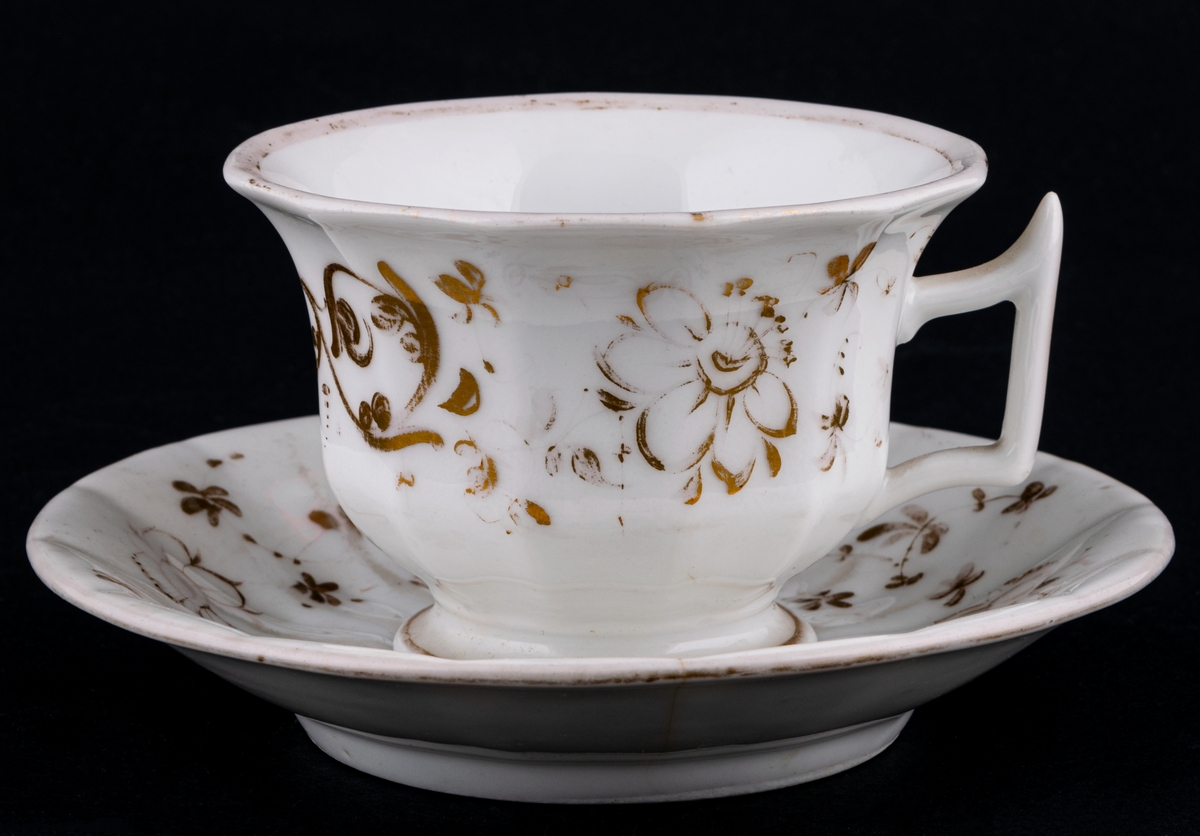 Kaffekoppar 5 st, med 6 st fat. Vitt gods med gulddekor av blommor och rocailler. Upptill utsvängd kopp, indragen mot foten. Uppsvängt öra, rakt avslutat nedåt. Uppsvängt fat.