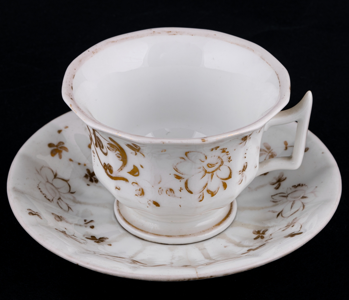 Kaffekoppar 5 st, med 6 st fat. Vitt gods med gulddekor av blommor och rocailler. Upptill utsvängd kopp, indragen mot foten. Uppsvängt öra, rakt avslutat nedåt. Uppsvängt fat.
