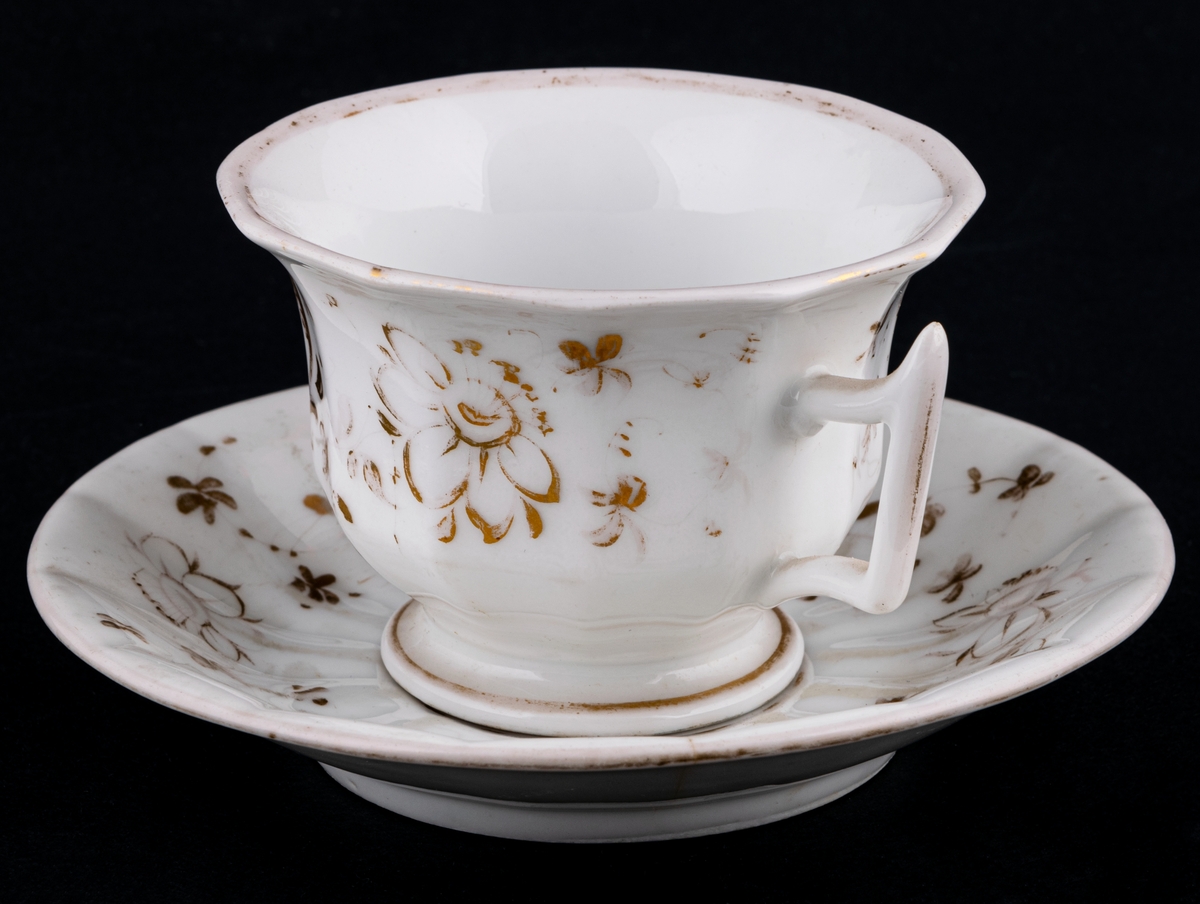 Kaffekoppar 5 st, med 6 st fat. Vitt gods med gulddekor av blommor och rocailler. Upptill utsvängd kopp, indragen mot foten. Uppsvängt öra, rakt avslutat nedåt. Uppsvängt fat.