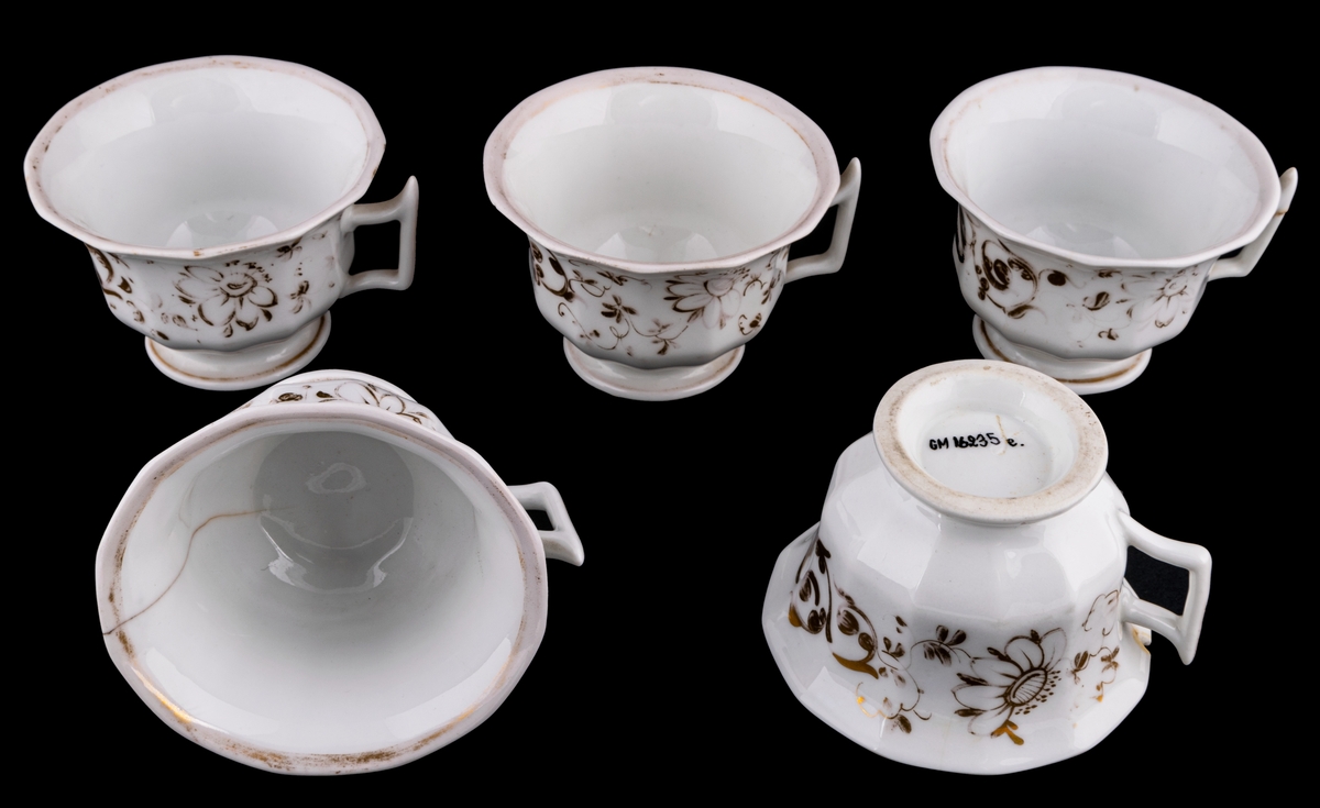 Kaffekoppar 5 st, med 6 st fat. Vitt gods med gulddekor av blommor och rocailler. Upptill utsvängd kopp, indragen mot foten. Uppsvängt öra, rakt avslutat nedåt. Uppsvängt fat.