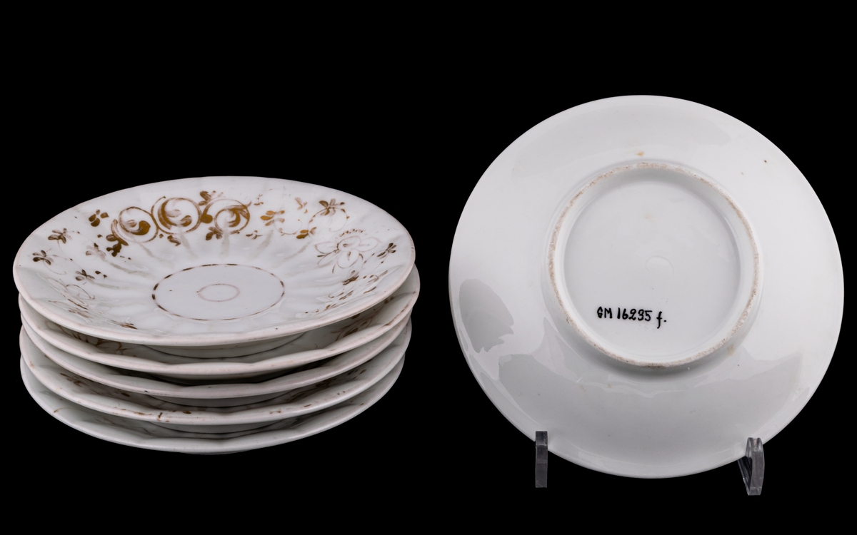 Kaffekoppar 5 st, med 6 st fat. Vitt gods med gulddekor av blommor och rocailler. Upptill utsvängd kopp, indragen mot foten. Uppsvängt öra, rakt avslutat nedåt. Uppsvängt fat.