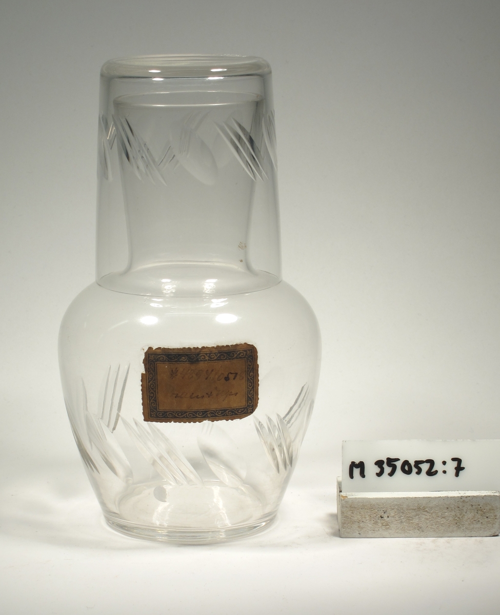 Ovoid med utvikt hals/mynning. Snedställda oliver och skär.

Karaffen samhör med vattenglaset M 35052:8