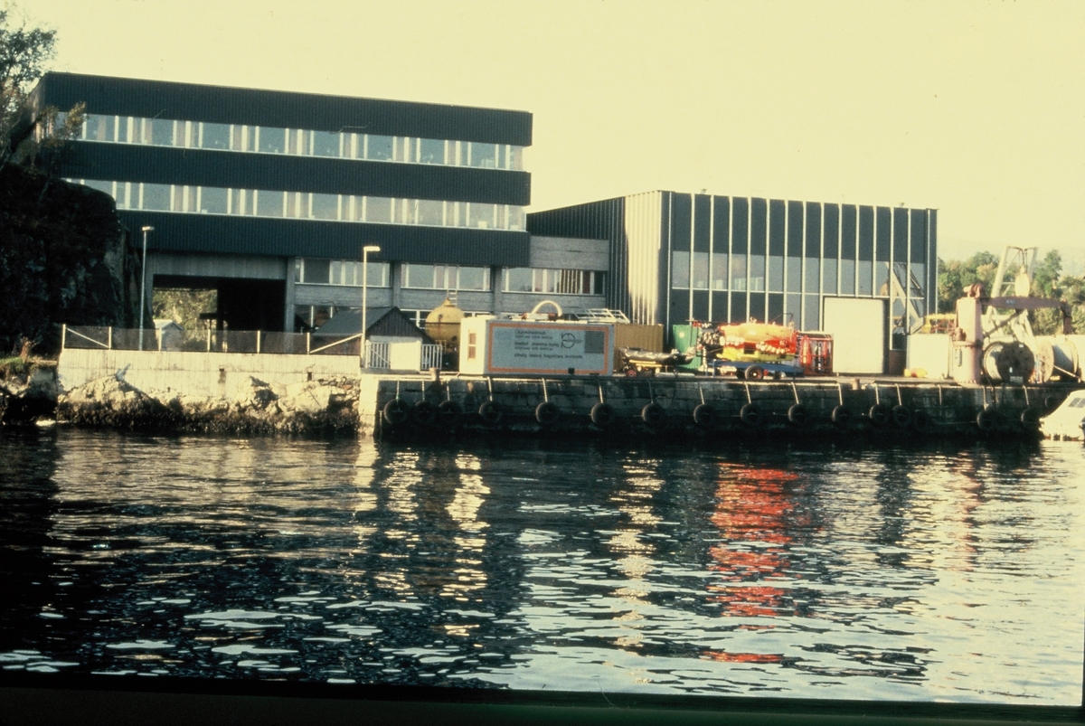 NUI, senere NUTEC utenfor Bergen, sett fra sjøsiden. På kaien står diverse utstyr, som konteinere, dykkerkammer og wirere.