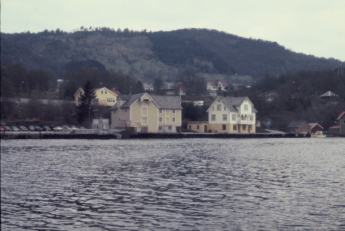 Kystlandskap sett fra sjøsiden. Bilde nr. 1 viser ei bygd med handel og parkeringsplass ved kaien.