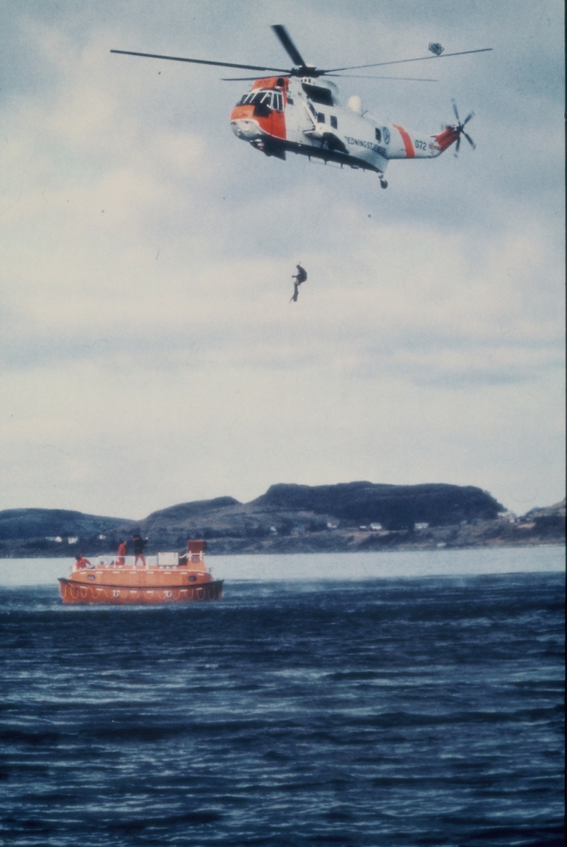 Redningsøvelse i en fjord på sørvestlandet. Et redningshelikopter sirkler over en livbåt med mannskap ombord. På bilde nr. 2 heises en livredder ned fra helikopteret.