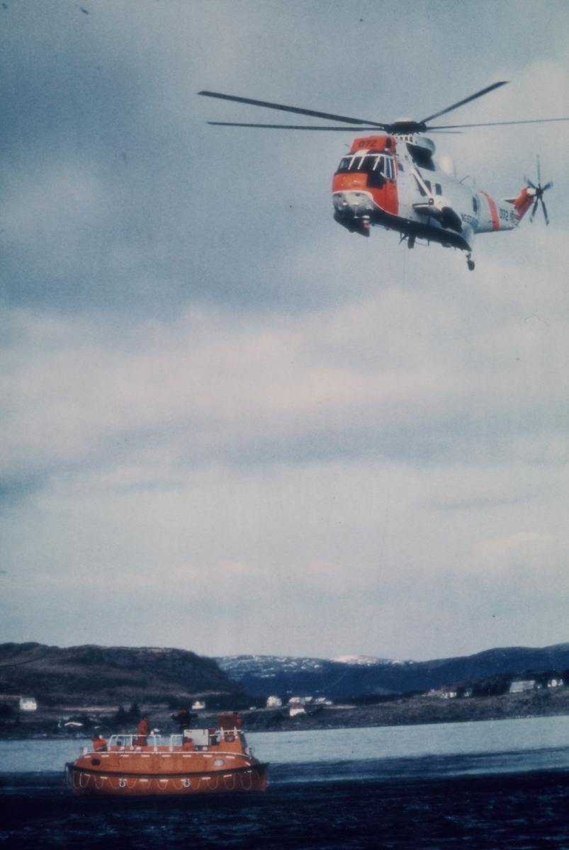 Redningsøvelse i en fjord på sørvestlandet. Et redningshelikopter sirkler over en livbåt med mannskap ombord. På bilde nr. 2 heises en livredder ned fra helikopteret.