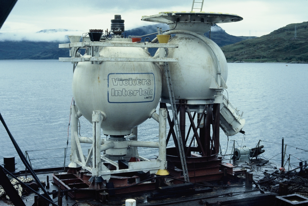 Moduler for et undervannsanlegg heises over kanten fra en båt eller lekter. Det står "Vickers Intertek Limited" på den ene modulen.
