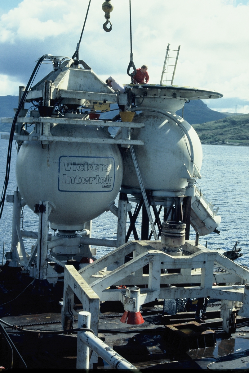 Moduler for et undervannsanlegg heises over kanten fra en båt eller lekter. Det står "Vickers Intertek Limited" på den ene modulen.