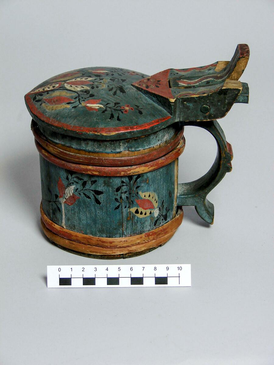 Dryckeskannor. A (brun): Dryckeskanna, av trä, laggad, med tre dubbelband. Konisk. Med lock. Gulfernissad. Locket med virvelstjärna i rött och grönt. Kring kannan nederst halvcirkelformiga, därovanför slingformiga och överst beslagsliknande ornament i rött, grönt och svart. Bottens undersida märkt m brännstämpel: M MS, inristat: IHD. Banden i rödbrunt. Diam(nedtill) 14,5 cm. H. 18,8 cm. Doroeta socken, Lappland. 
B Drickeskanna, av granträ, laggad. Ett band övriga bortfallna. Snidat trähandtag i svängda former. Propp överst i buktiga locket, bortfallen. Mörkgrön färg med blomdekor i rött, svart, vitt. Målningen delvis hårt sliten. Undertill ristat klumpigt BLD. Höjd 16 cm., diam. 13 cm. Inköpt av fru Johansson, Härnösand, april 1917, från Dorotea socken, Lappland. 
C (blå): Dryckeskanna av trä. Laggad, cylindrisk. Försedd med 4band placerade 2 och 2. Lodgrepe, överst med tumgrepp samt gångjärn till locket. Grepen har eventuellt haft 2 grepp varav det yttre(?) är avbrutet. Locket är cylindriskt med konvex ut- och konkav insida. Framtill är en liten spets utdragen. Bottnen är fäst i fasat spår i stavarnas nederdel. Blåmålad med stiliserade blommor i beige, gult och rött på svarta kvistar. Banden och lockets kant är röda. Brännstämpel på undersidan: Ett konstigt E med prickar över. 